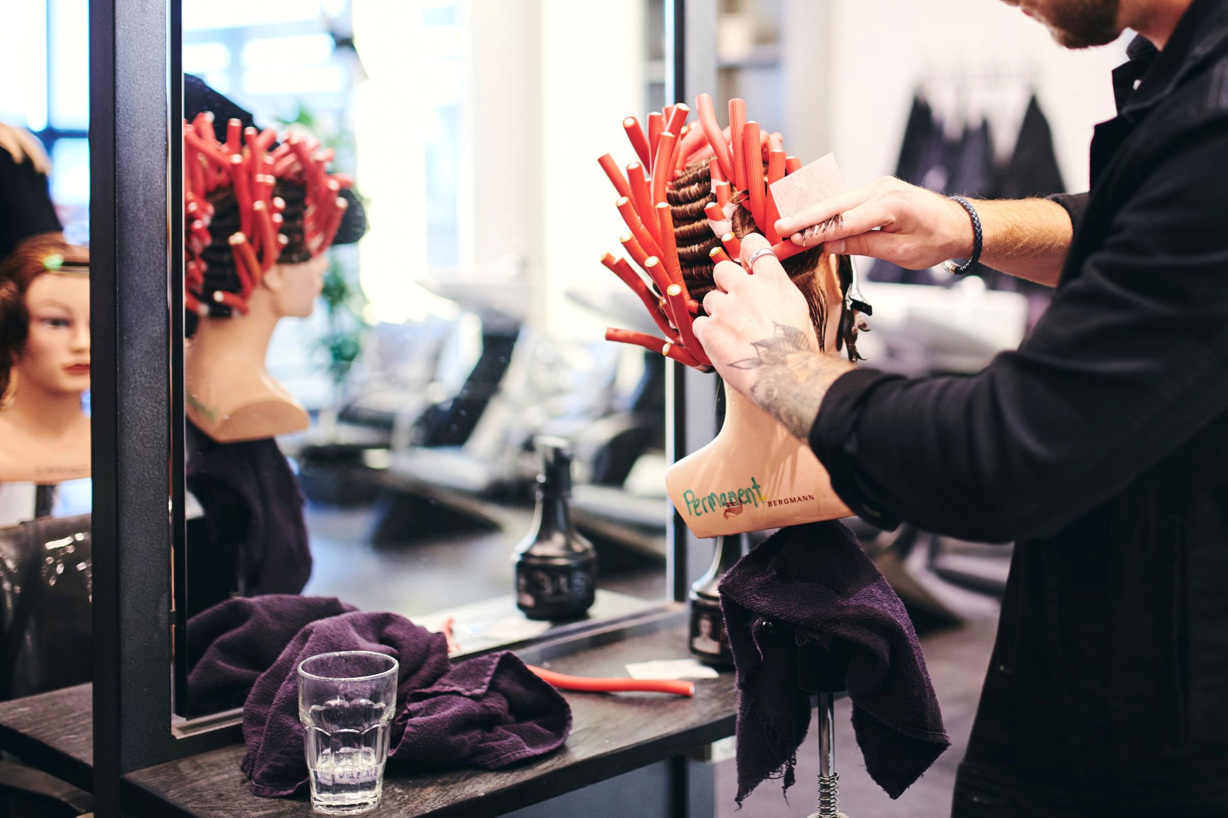 En mandlig frisørelev på Hansenberg ruller skumspoler i håret på et øvelseshoved.