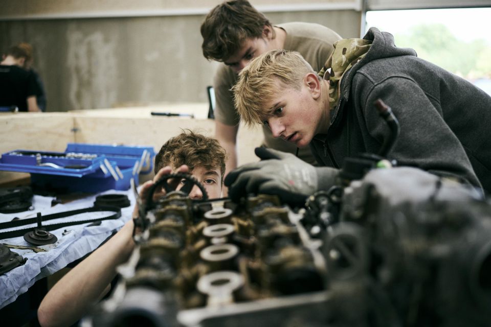 Tre mekanikerelever på Grundforløb 1 nærstuderer en motor på et af skolens værksteder.
