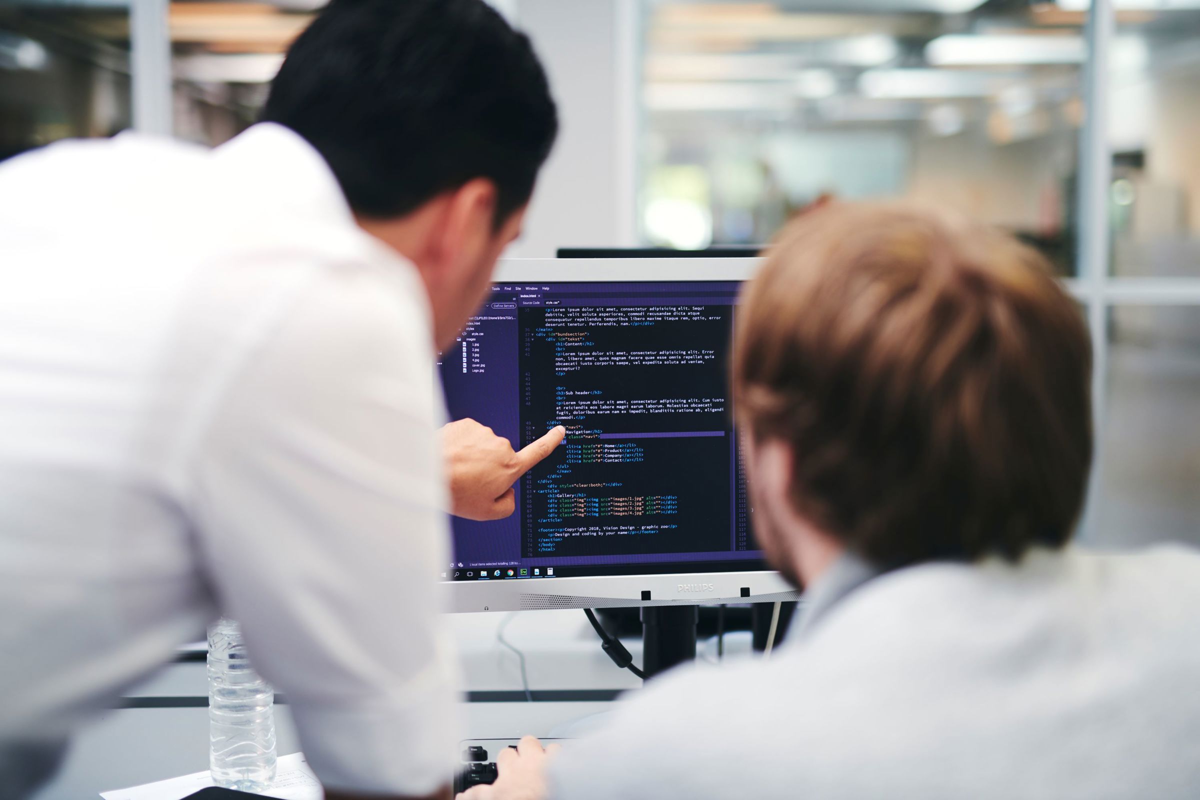 En lærer underviser en webudviklerelev i kodning på en computerskærm.