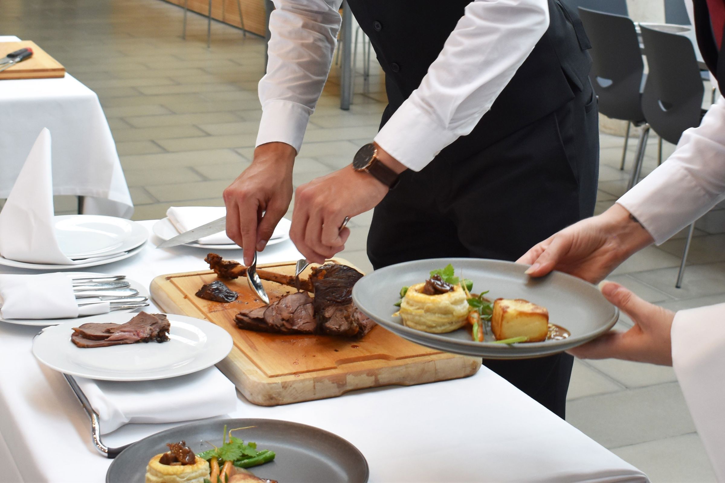 To tjenerelever anretter maden på smukkeste vis til tallerkenservering.