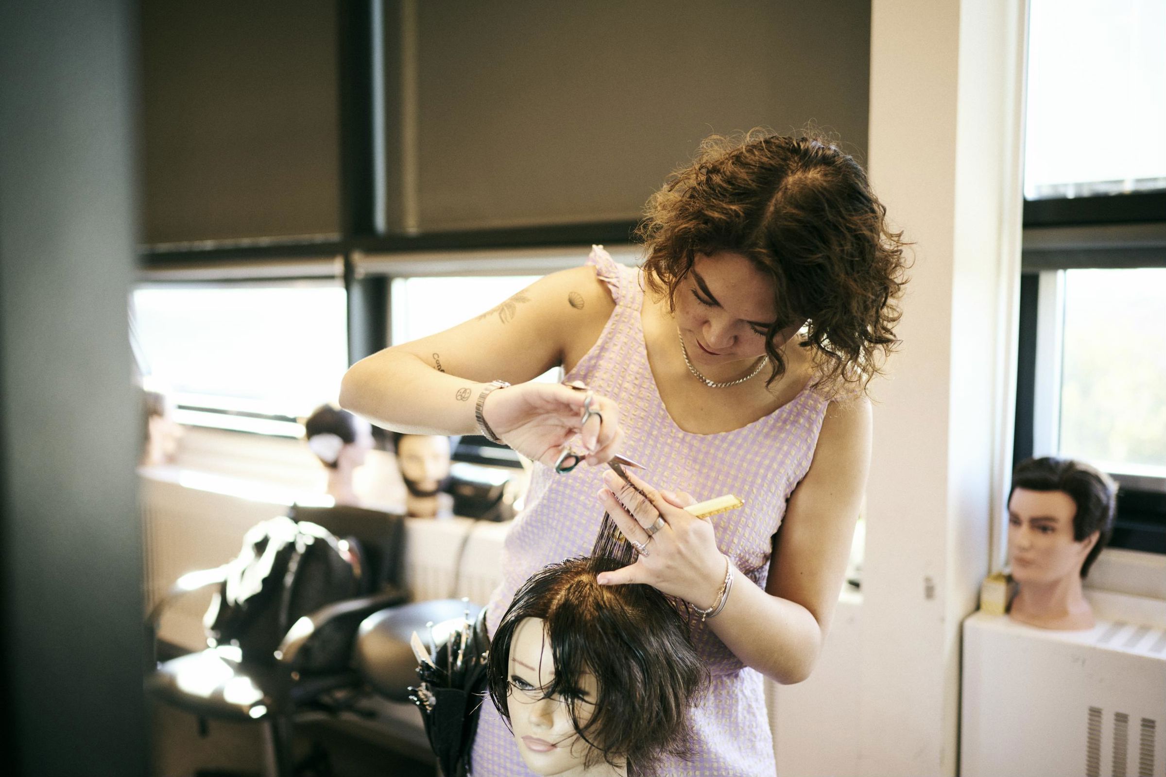 Frisørelev på Hansenberg klilpper hår på et øvelseshoved.