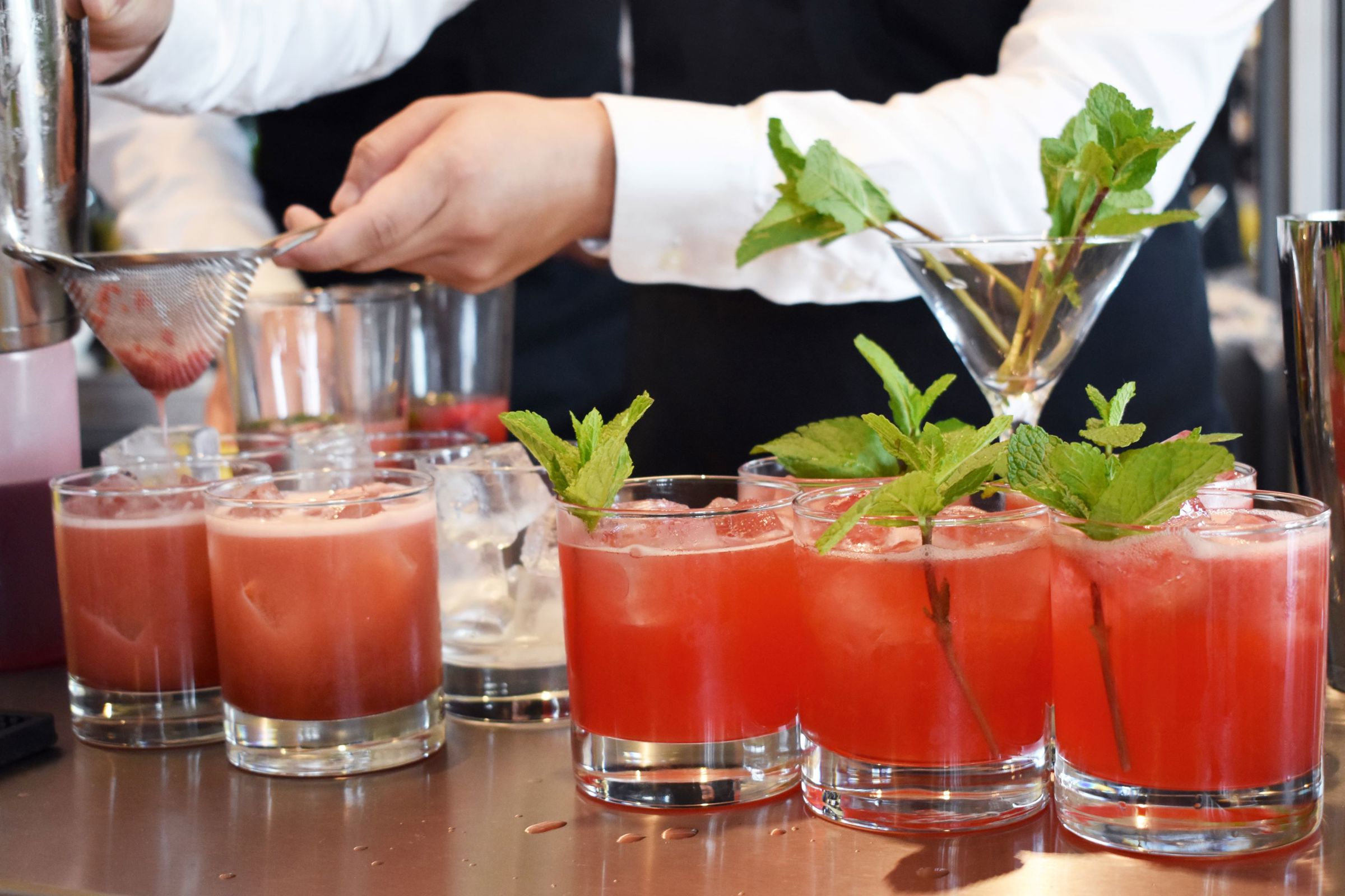 En tjenerelev mixer flotte røde drinks med en kvist af mynte som pynt på Hansenberg.