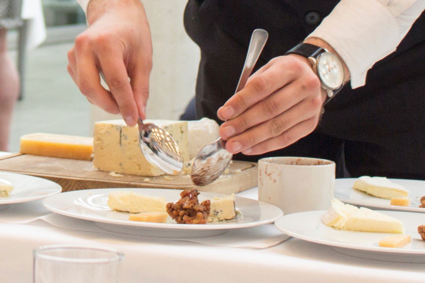En tjenerelev anretter nogle delikate ostetallerkner til servering for gæsterne.